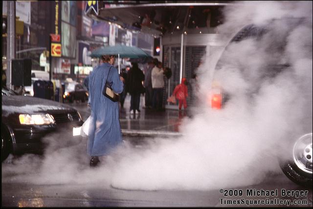Steam rises as pedestrian crosses W. 44th St. and Broadway during a heavy summer rain in Times Square. 2002.