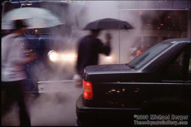 Steam rises as pedestrians cross W. 44th St. and Broadway during a heavy summer rain in Times Square. 2002.